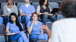 Students in scrubs sit in an auditorium listening to a lecture on new digital healthcare and patient care software.
