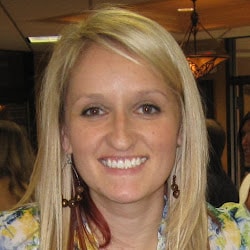 A smiling person with long blonde hair and large earrings in an indoor setting.