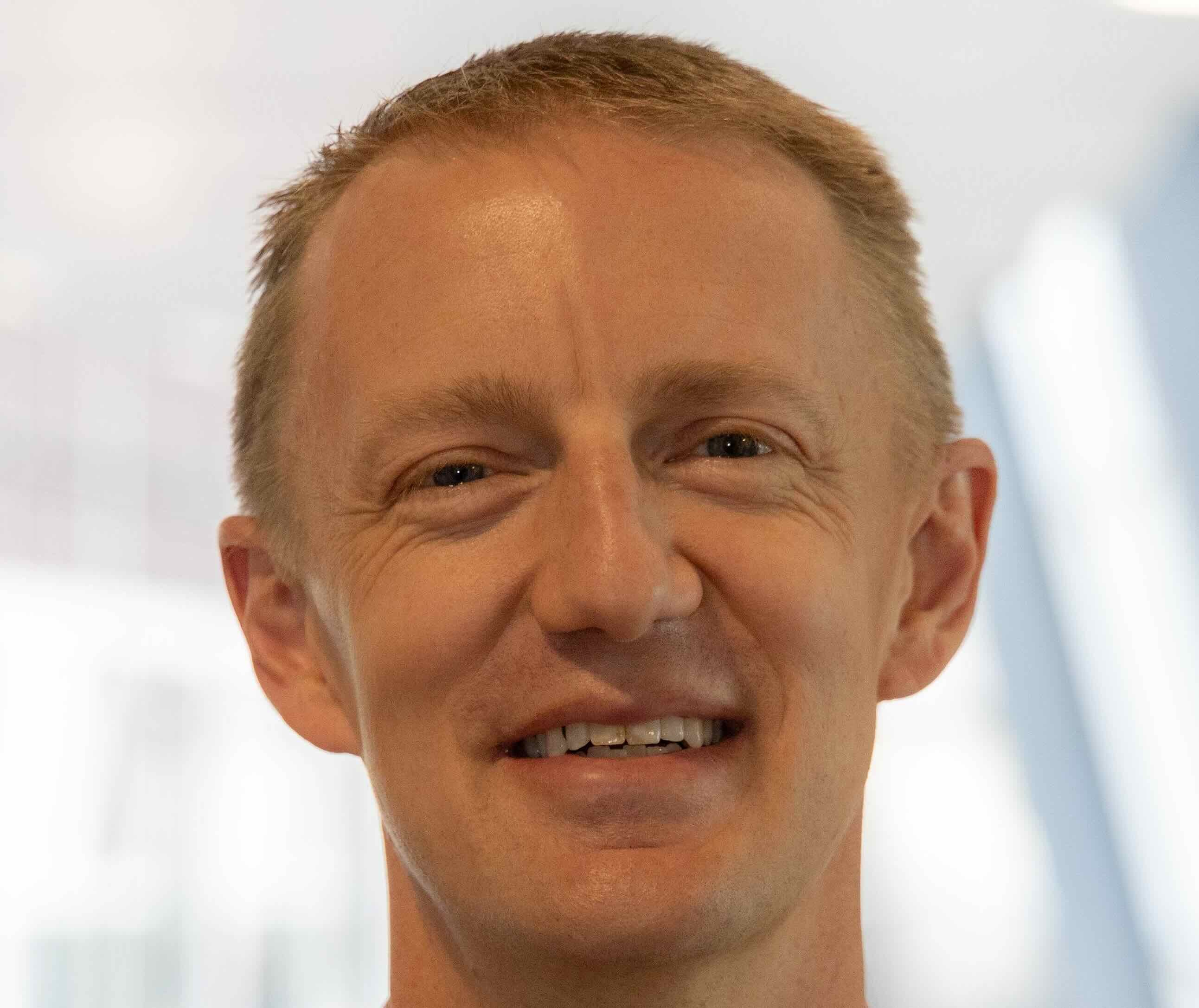 A man with short light brown hair smiles at the camera indoors, illustrating the future of healthcare education with medbridge.