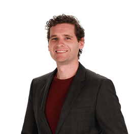 A curly-haired person in a black blazer and red shirt smiles against a neutral background.