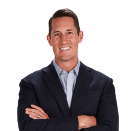 Man in dark blazer and light shirt smiling with arms crossed, against a plain white background, for medbridge.