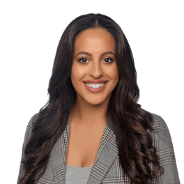 A smiling person with wavy brown hair and a plaid blazer against a white background, used for medbridge profile.