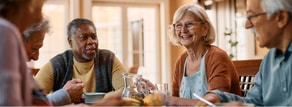 Four older adults sit at a table eating and talking about healthcare education in a bright indoor space, with Medbridge materials present.