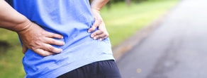 A person in a blue shirt stands on a path, holding their lower back, illustrating pain recognition for medbridge healthcare training.