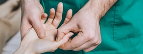 A healthcare professional in green scrubs examines a patient's thumb using Medbridge digital tools.