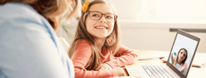 A girl with glasses and a yellow bow smiles during a medbridge patient care software video call.