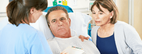 A patient listens to a nurse discussing digital healthcare benefits, with a woman observing nearby, highlighting Medbridge.