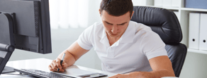 A man in a white shirt uses a tablet and stylus at his desk, exploring Medbridge's digital healthcare software.