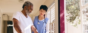 A healthcare worker uses Medbridge software while helping an elderly man with a walker.