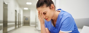 A tired person in blue scrubs sits in a hallway, overwhelmed by healthcare education and Medbridge software.
