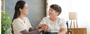 A young woman smiles as she holds the hand of an older woman in a wheelchair, symbolizing compassionate digital healthcare through medbridge.