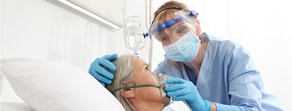 A nurse in PPE adjusts an oxygen mask on a patient, highlighting digital tools and improved training like medbridge.