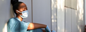 A healthcare worker in scrubs and a mask rests against a wall, embodying medbridge's dedication in digital healthcare.