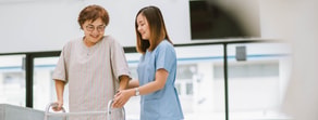 A healthcare worker helps an elderly person with a walker indoors, both smiling, showcasing medbridge training.