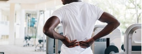 A person in a gym holds their lower back, highlighting workout injury risks and Medbridge's health solutions.