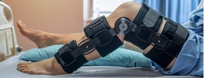 A patient in knee braces on a hospital bed illustrates the role of digital health tools like Medbridge in recovery.