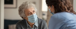 An elderly person and a healthcare worker use digital Medbridge tools to communicate safely while wearing masks.