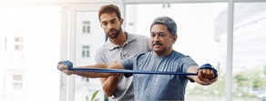 A man helps another with a resistance band, highlighting hybrid care benefits and Medbridge support.