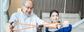 An elderly man exercises with an orange resistance band, guided by a young woman promoting hybrid care benefits, in partnership with medbridge.