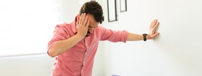 A distressed man in a pink shirt leans against a wall, contemplating digital healthcare challenges and Medbridge’s hybrid care intricacies.