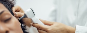 A healthcare professional uses Medbridge software to examine a patient's ear with an otoscope.