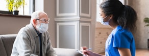 An elderly man and a nurse discuss Medbridge patient care software on a sofa.