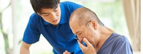 A younger person helps an older person, with the older individual writing on a paper.