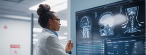 A lab coat-wearing professional reviews brain scans on a monitor, highlighting hybrid care in digital healthcare, as exemplified by medbridge.