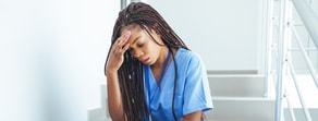 A nurse in blue scrubs sits wearily on the stairs, highlighting the need for flexible solutions like medbridge's hybrid care to reduce healthcare fatigue.