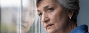 A woman with gray hair looks out a window, reflecting on her commitment to healthcare and Medbridge's hybrid care model.