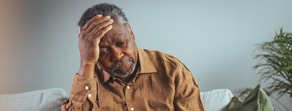 A man sits on a couch, looking thoughtful, likely pondering hybrid care or medbridge healthcare education.