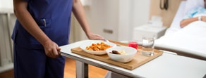 A healthcare worker uses Medbridge software to deliver a meal tray to a patient in a hospital bed.