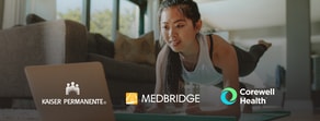 A woman planks indoors, following a digital healthcare routine on her laptop with logos for Kaiser Permanente, medBridge, and Corewell Health displayed.