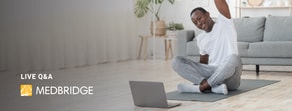 A person does yoga in front of a laptop, possibly using medbridge for wellness guidance.