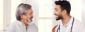 An older man smiles at a Medbridge professional with a stethoscope, highlighting digital healthcare benefits indoors.