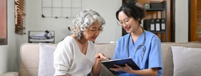 A nurse in blue scrubs discusses healthcare education with an older woman.