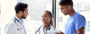 Three medbridge professionals, one in a white coat and two in scrubs, discussing in a bright room.