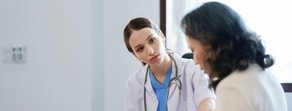 A healthcare professional in a white coat uses patient care software in an office to discuss modern digital healthcare strategies with a patient.