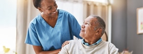 A nurse in a blue uniform comforts an elderly man in a well-lit room.