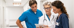 Three healthcare professionals in scrubs examine patient care software on a tablet, showcasing medbridge hybrid care.