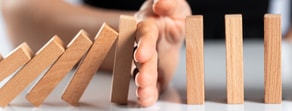 A hand stops falling dominoes, representing precision and control in medbridge healthcare training.