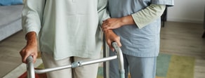 A person using a walker is assisted by someone in scrubs indoors, showcasing medbridge healthcare training.