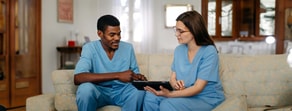 Two healthcare professionals in blue scrubs sit on a sofa, reviewing a tablet with medbridge content.