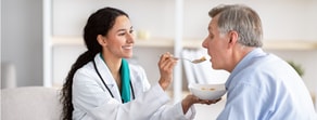 A healthcare provider uses medbridge technology while feeding an elderly man at home.