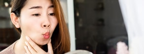 A person with long hair makes a playful fish face in a mirror, pondering digital healthcare and medbridge.