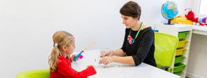 A woman and child play a fishing game at a table, with toys and a globe in the background.