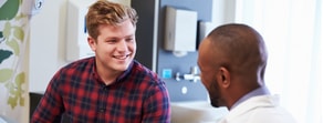 A man in a plaid shirt discusses digital healthcare with a person in a medical coat at medbridge.