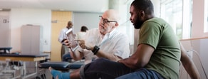 Two men sit on medical tables discussing patient care software on a digital tablet with medbridge.