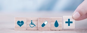Wooden blocks with healthcare icons are lined up, with a hand placing the medical cross block, representing medbridge's impact on patient care.