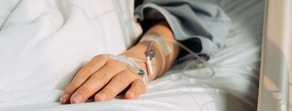 A hand with an IV drip lies on a white hospital bed, highlighting medbridge's role in modern healthcare.